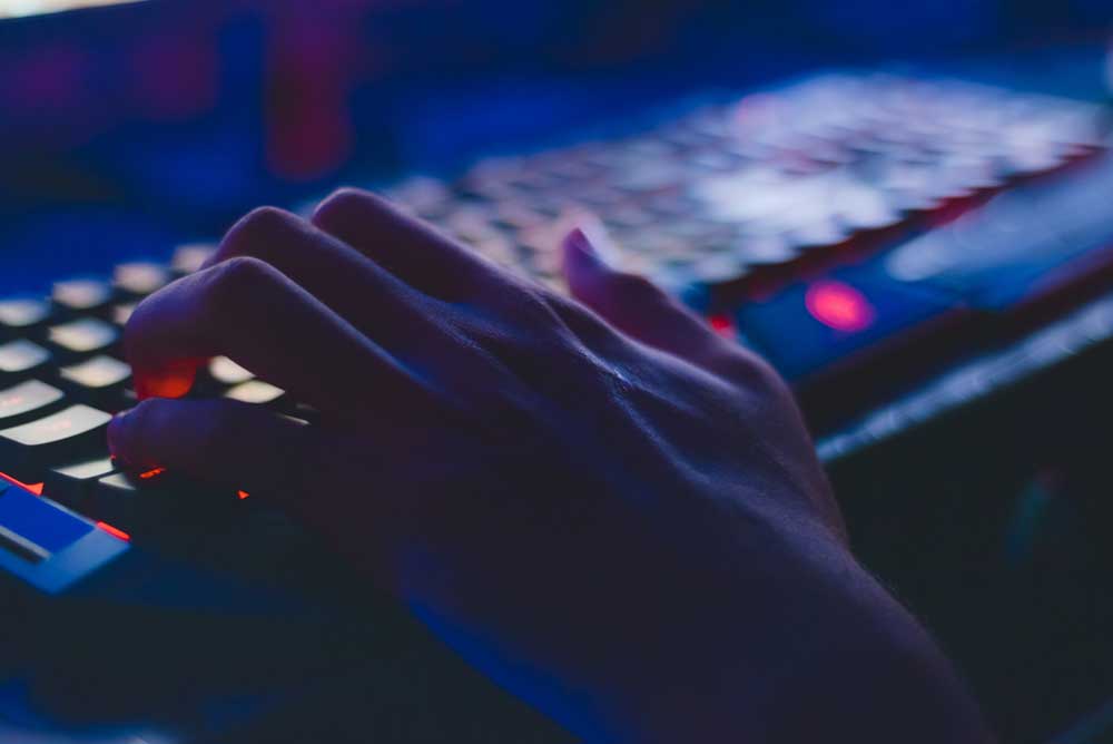 Close up of a hand typing on a keyboard in a dark room. 