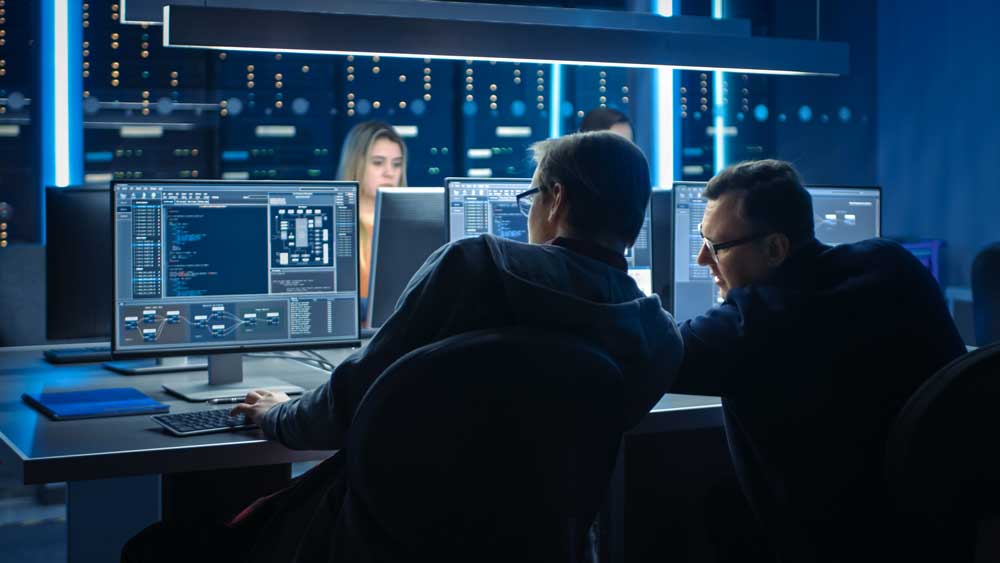 Four cybersecurity professionals in front of their monitors, looking at data. 