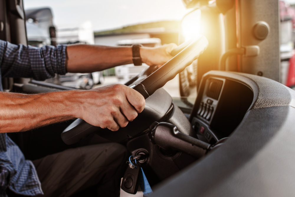 Inside of a semi, a man has his hands on the wheel. 