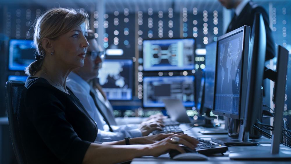 with the growing cybersecurity skills gap, there's less trained professionals for organizations to hire. Inside of a security operations center, a man and woman are working 