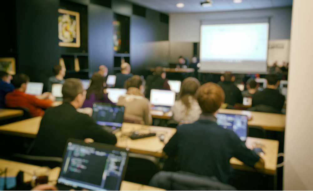 In a classroom, a group of students are in front of computers at their individual desks. 