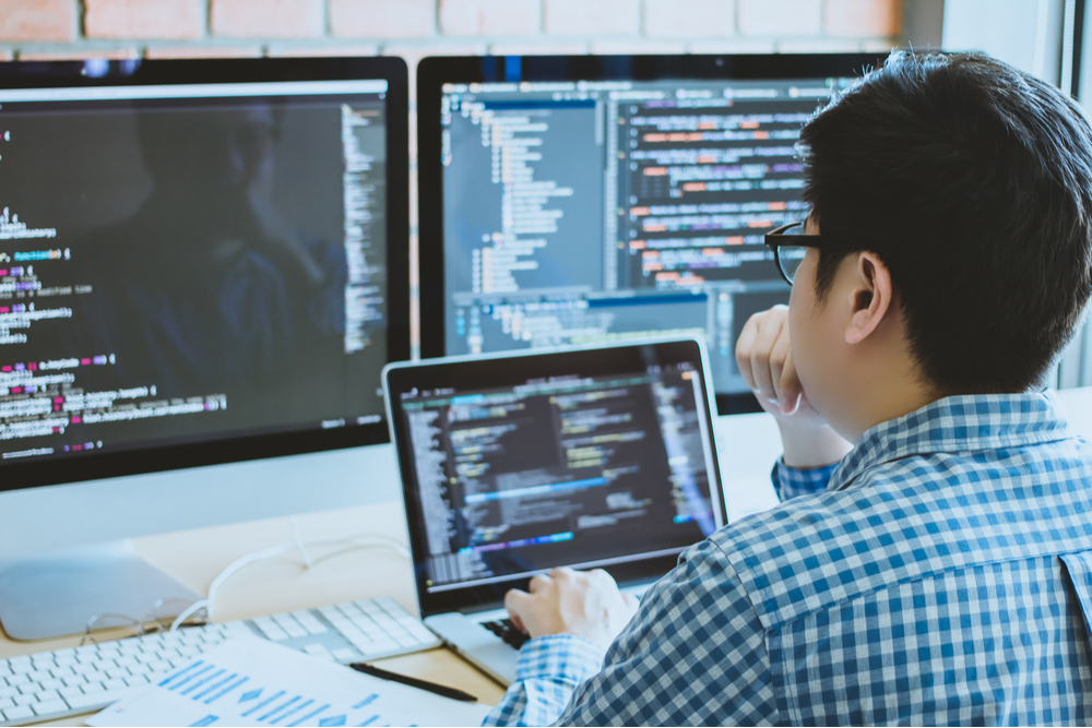 Sensitive data exposure is one of the top 10 risks of OWASP. A man it looking at a series of code on his computer monitors. 