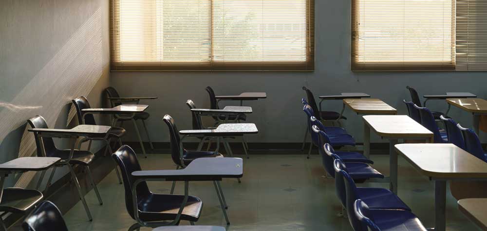 An empty classroom with the sun shining in on rows of desks. 