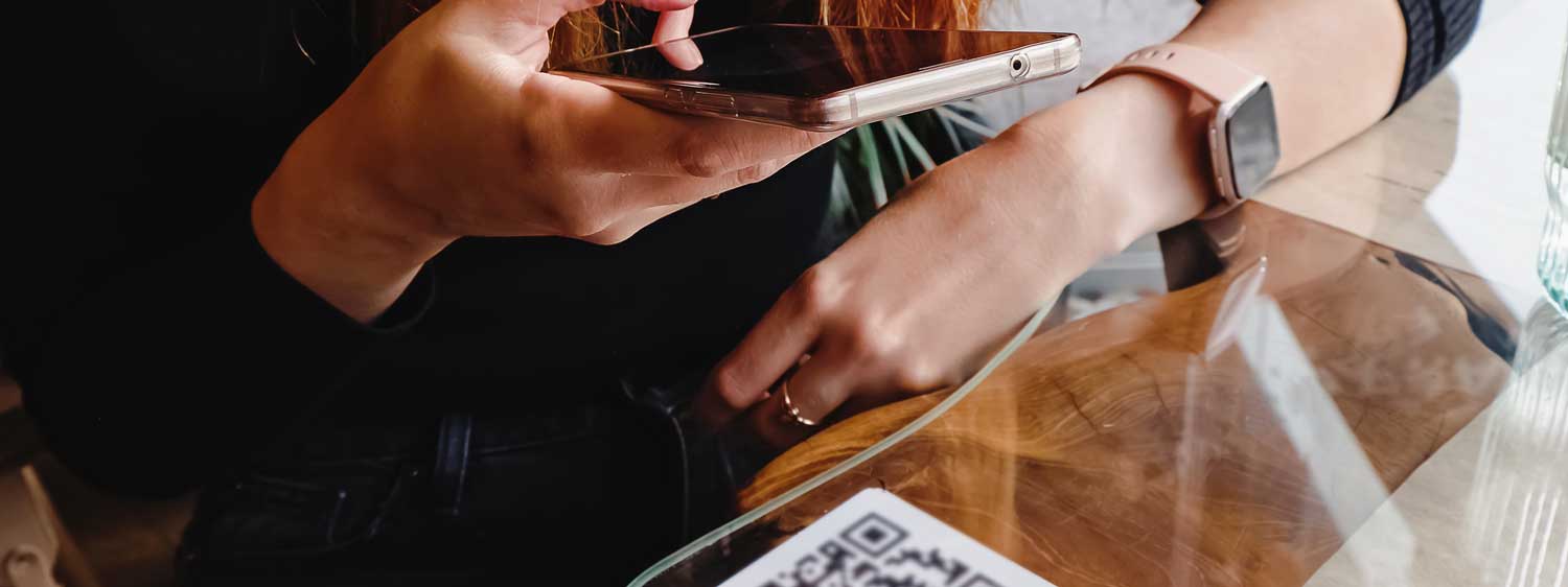 A woman holding a phone scanning a QR code on a restaurant table. 
