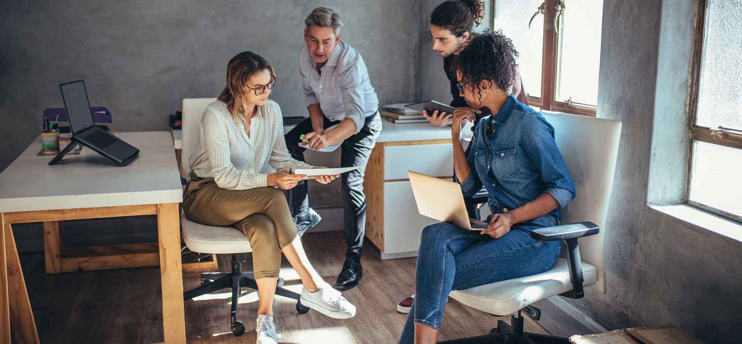 Four employees inside of an office, looking over some papers. 