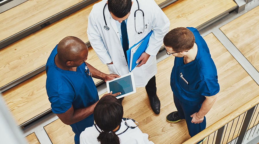 Image from above of two doctors and two nurses gathered around discussing, one of them holding a tablet